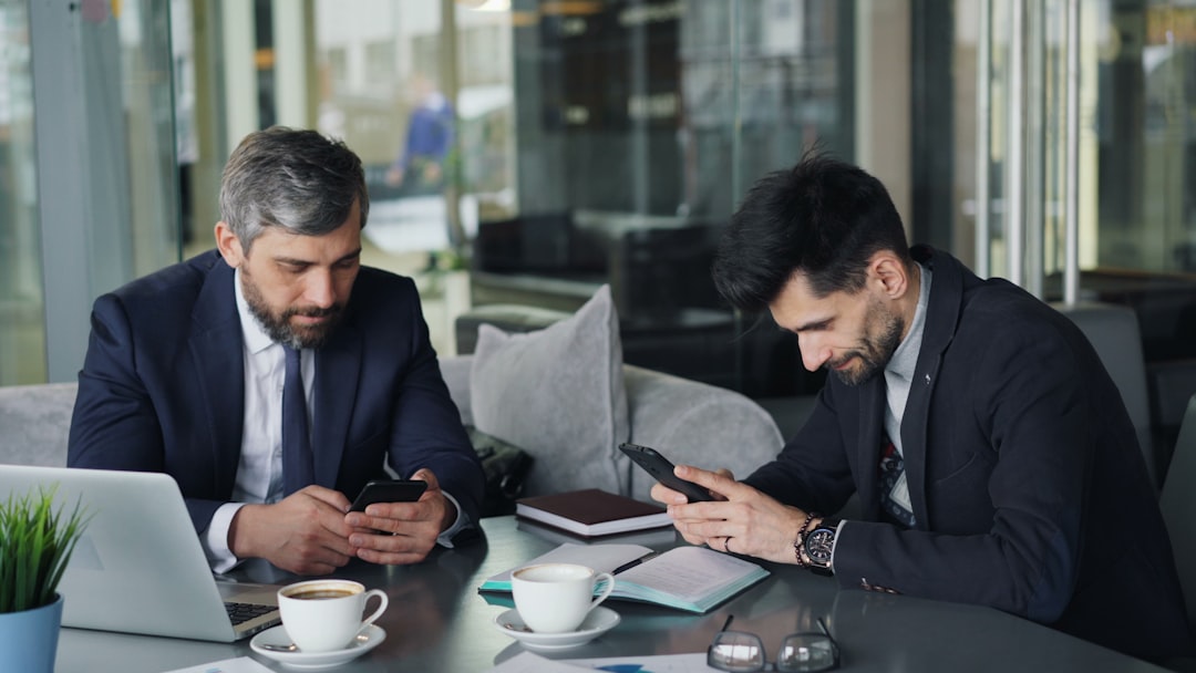 two-men-sitting-at-a-table-looking-at-their-phones-ihdtnyxv6ai